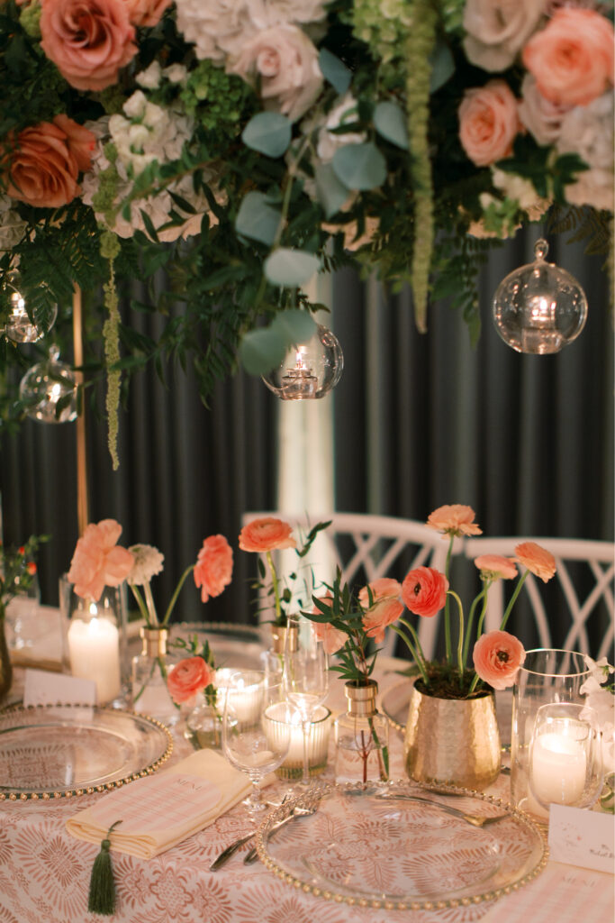 Experience the elegance of a table setup at The Tillinghouse in NJ, featuring a stunning floral arrangement with pink and white blooms, enchanting hanging glass orbs, lit candles casting a soft glow, and meticulously arranged place settings.